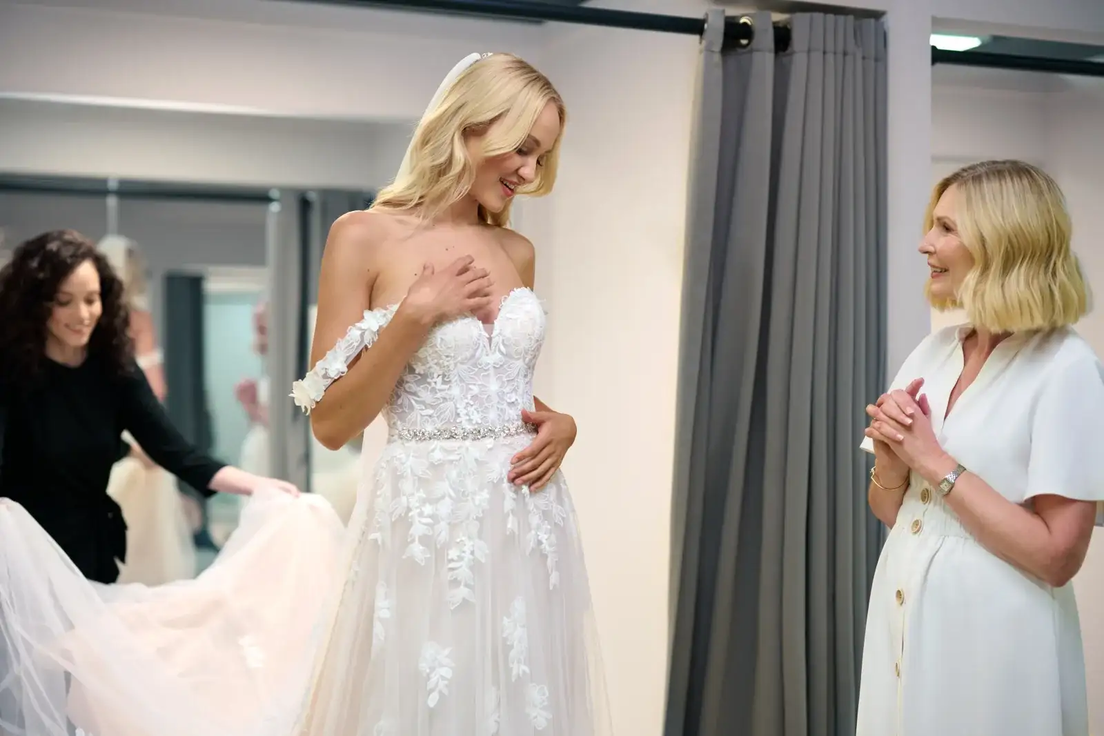 Bride looking at herself in a wedding dress while sharing the moment with her family.