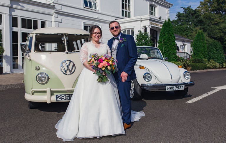 Bride and groom stood next to VW camper and VW beetle wedding vehicles