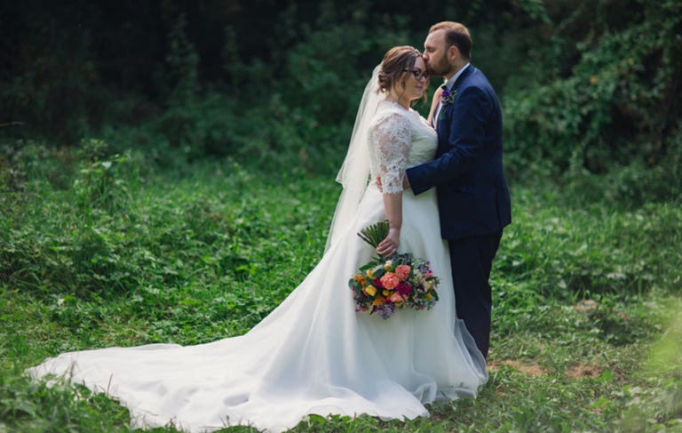 Bride and groom stood together in green meadow embracing