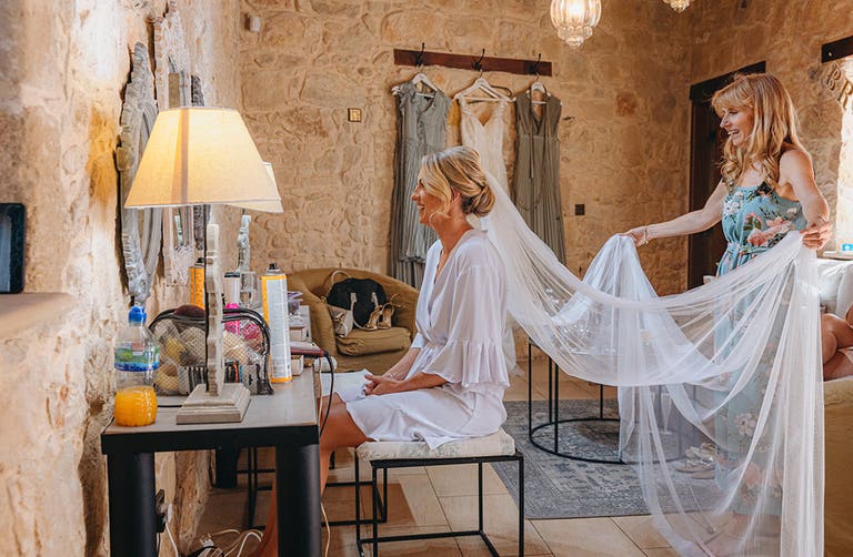 Bride Katie sitting while her bridesmaids fans out her bridal veil