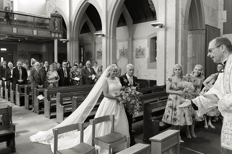 Bride walking down the aisle with her effortless veil trailing behind