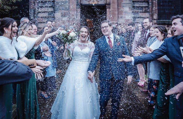 Rhiannon and Edward walking out of their wedding ceremony to their guests throwing confetti
