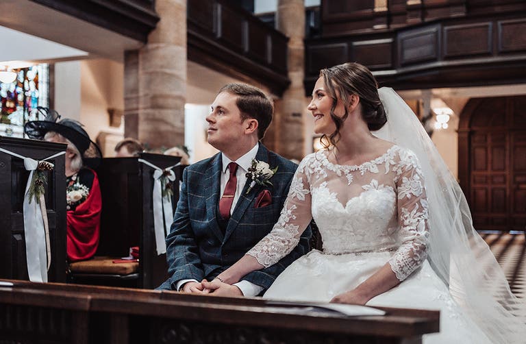 Rhiannon and Edward holding hands while sitting during their wedding ceremony