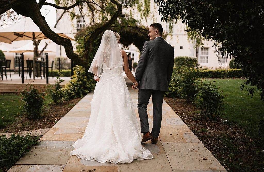 Sophie and Dean holding hands and looking at each other outside their wedding venue
