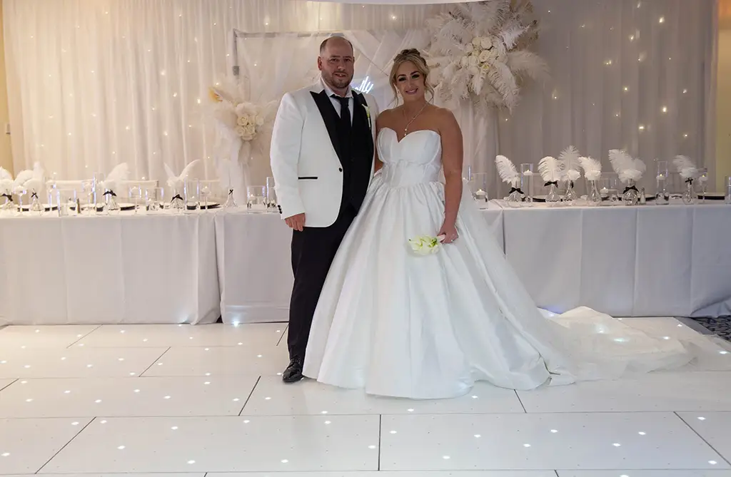 Rachel and Andrew posing in front of their wedding top table at their hotel wedding reception