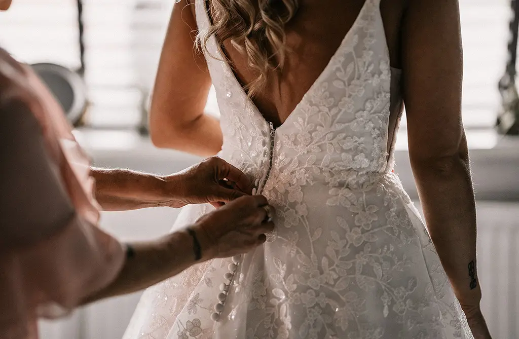 Close-up of bridal gown buttons being fastened on the back of Sophie’s wedding dress