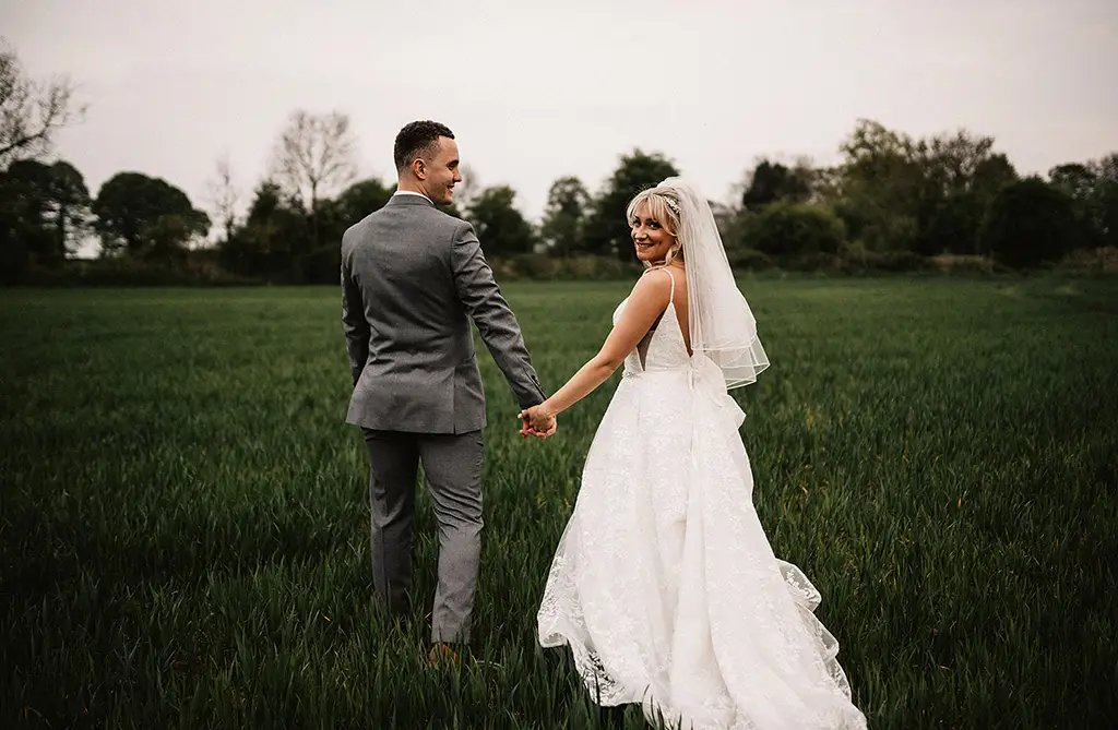 Sophie and Dean holding hands in a field looking back at the camera