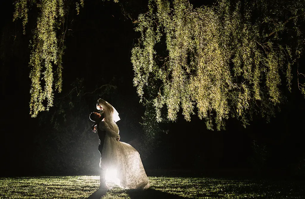 Dean lifting Sophie outside their wedding venue in the evening with strong lighting