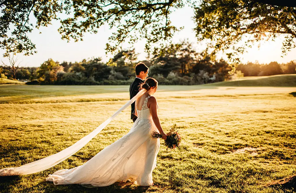 Gina and Elliot walking through fields at sunset during their spring wedding