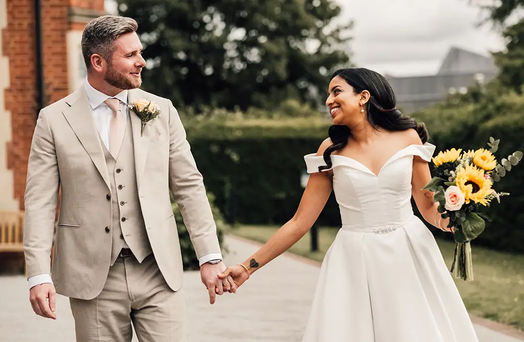 Pooja and Sam holding hands and smiling at each other on their wedding day