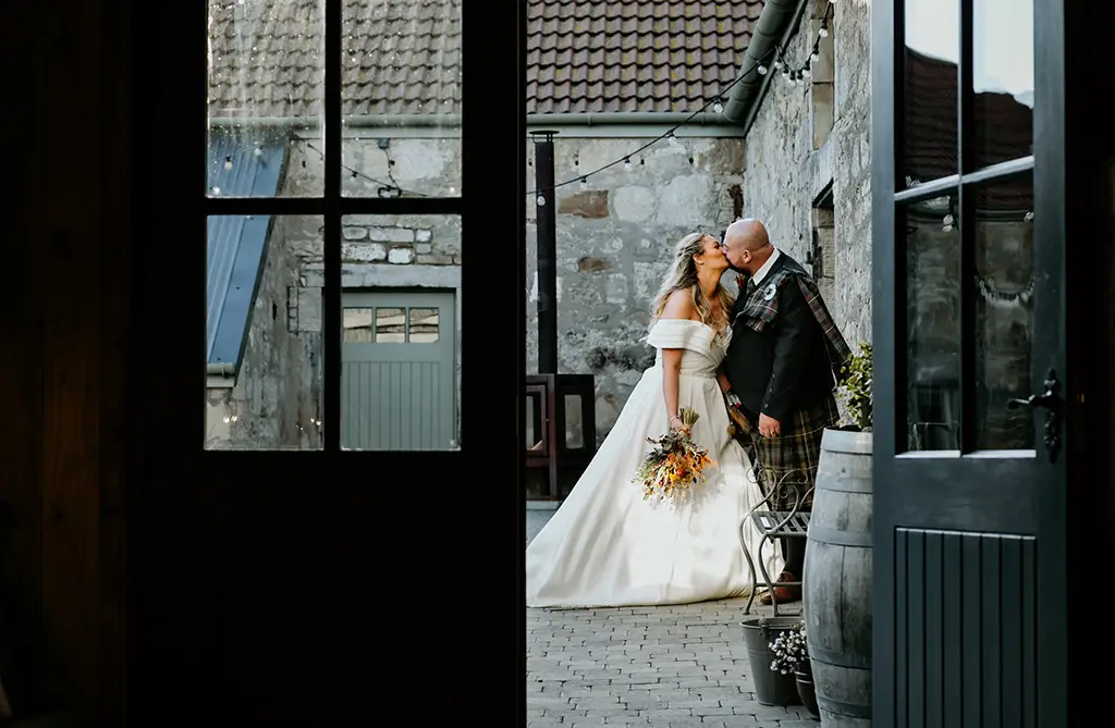 Michelle and Shaun kissing outside their wedding venue surrounded by countryside scenery
