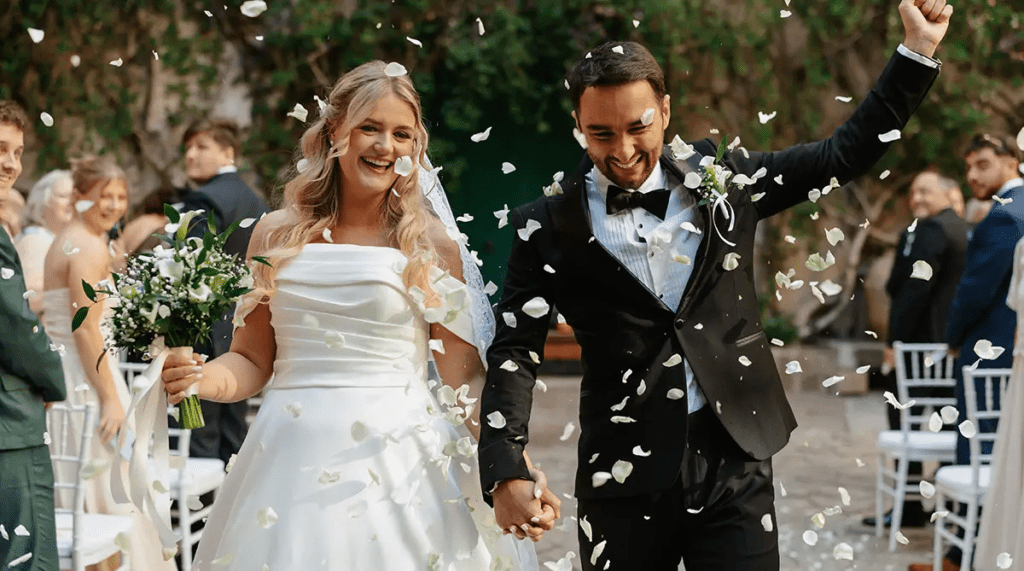 Georgia and James walking back up the aisle through confetti after their ceremony