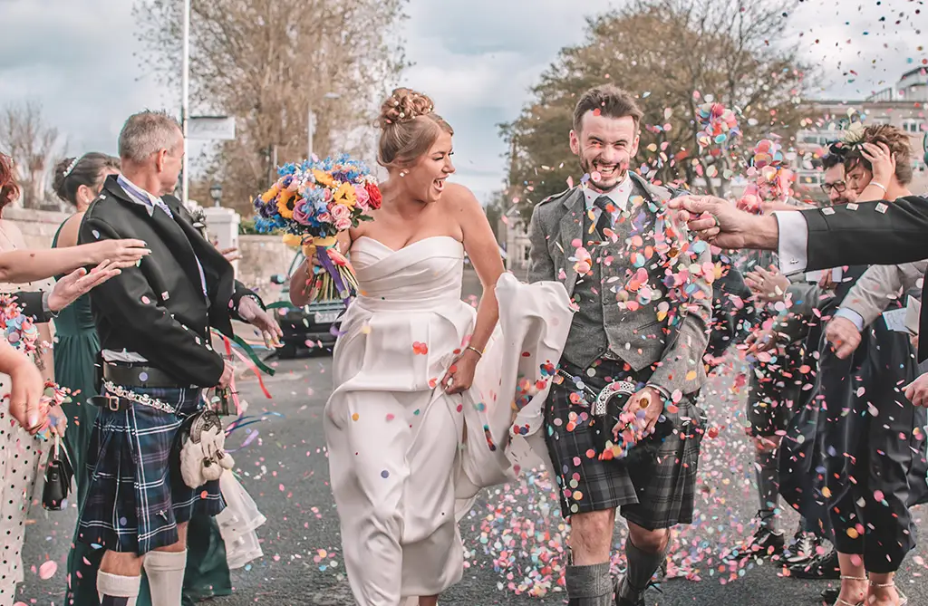 Daisey and Kieran walking outside as guests throw confetti