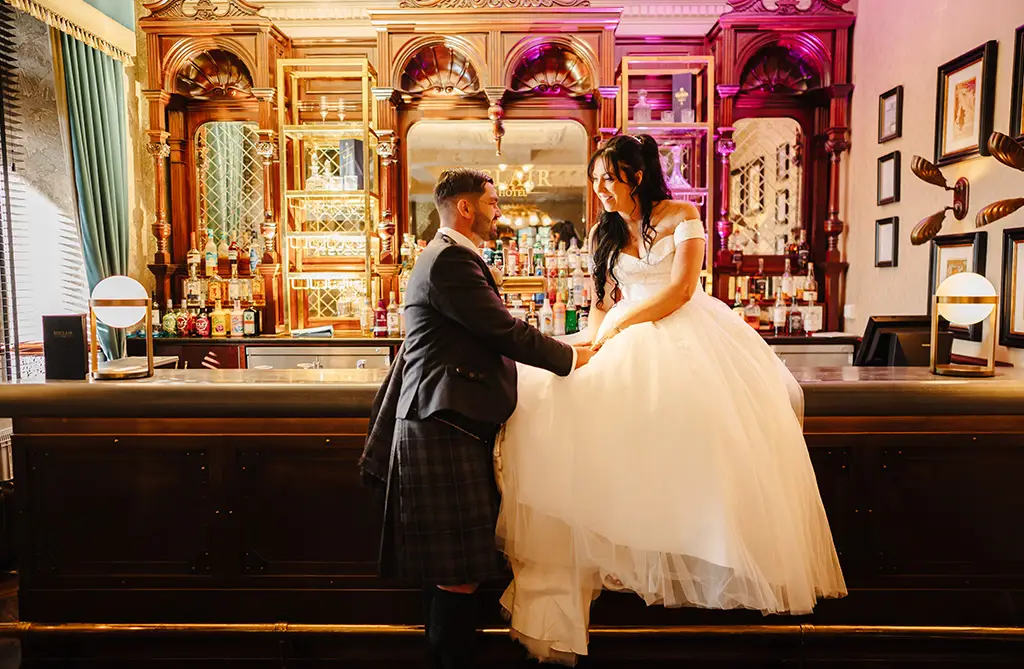 Kristeen and Ryan at their wedding with Kristeen sitting on the bar holding Ryan’s hand