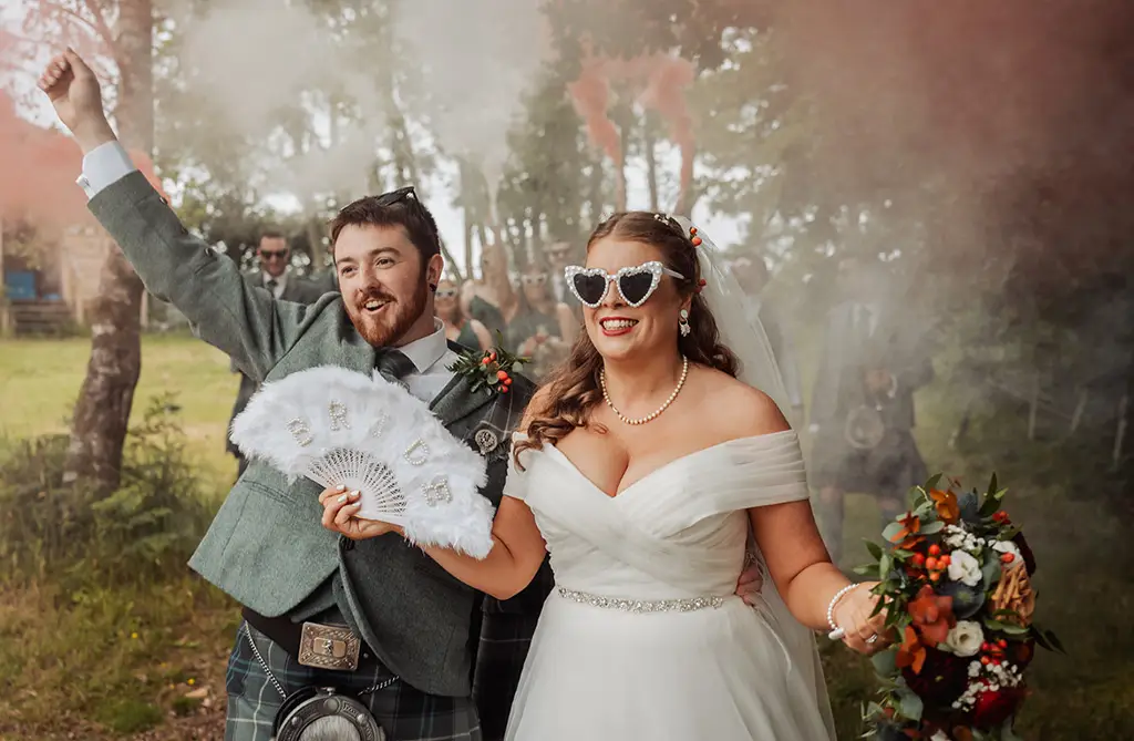 Sarah-Jane and Stephen wearing sunglasses as Sarah-Jane holds her fan and bouquet