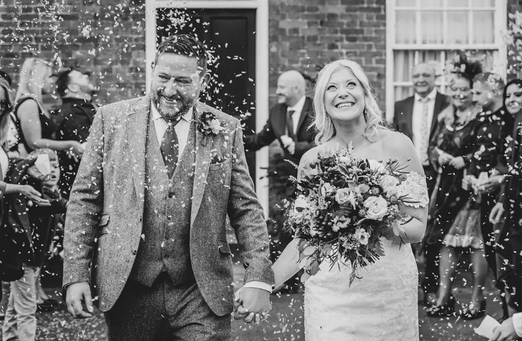 Black and white photo of Michelle and James with guests throwing confetti on their wedding day