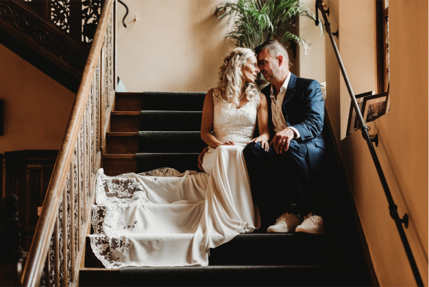 Ilse and Peter sitting on indoor stairs with their foreheads touching on their wedding day
