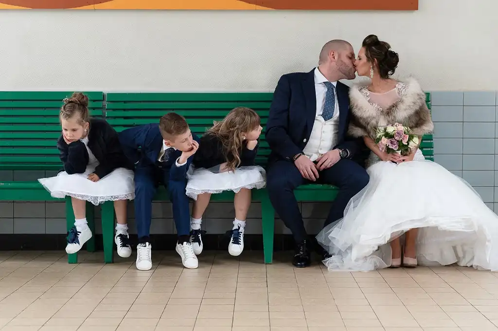 Kimberley and Hans kissing on a bench while their children watch during their wedding day